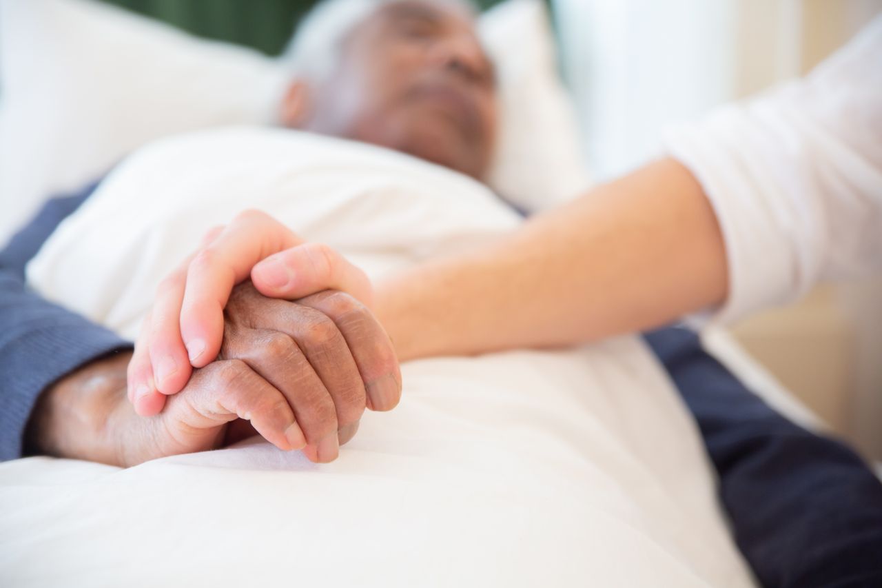 Hand hält die Hand eines im Bett liegenden Menschen